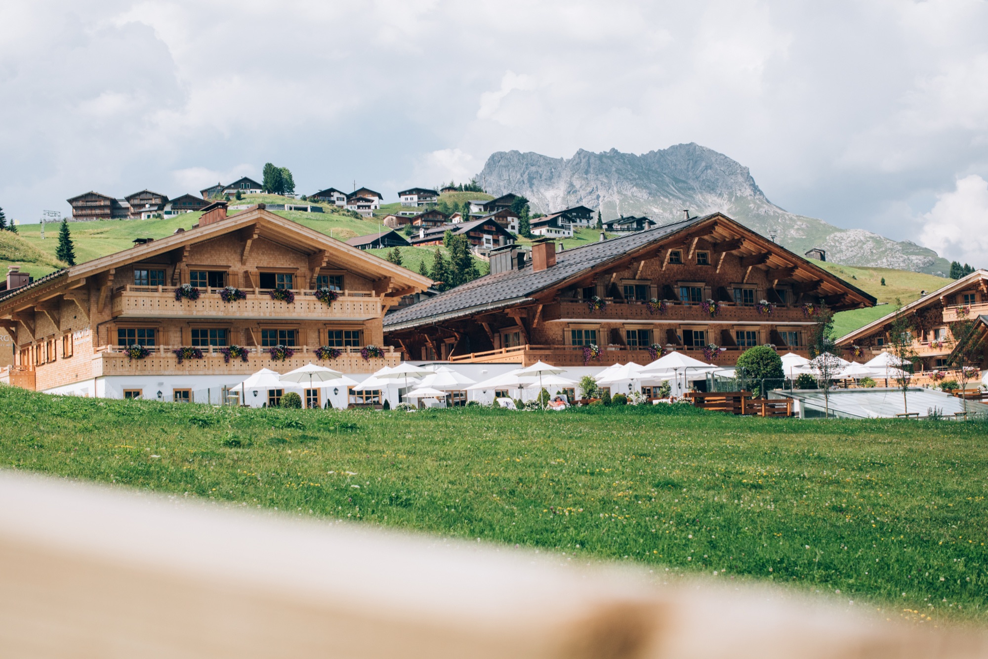 Grüne Almwiese und Chalets über dem sommerlichen Lech am Arlberg